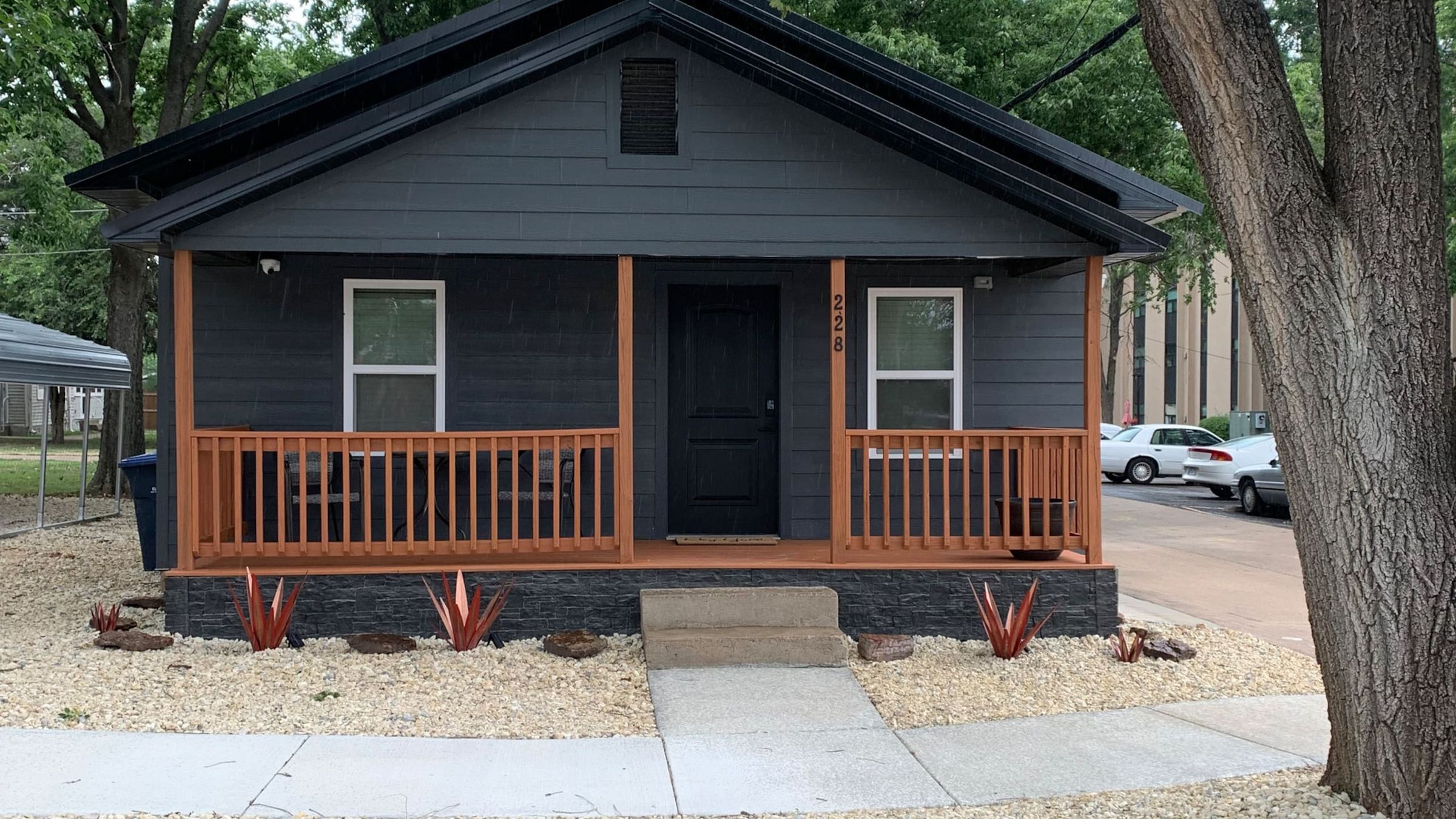 Rustic Roost: a dark gray cottage with a cedar-railed front porch under a big shade tree